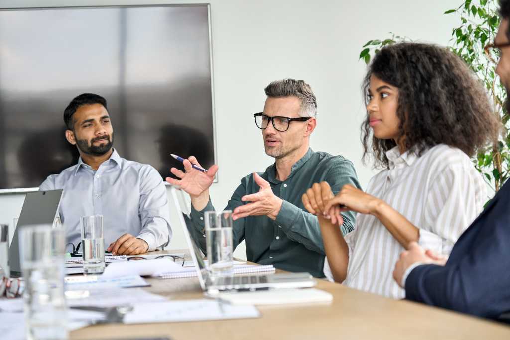 Mature mentor manager speaking at executive team meeting in boardroom. Male leader training executive team at board briefing. Multicultural professional business people discussing strategy in office